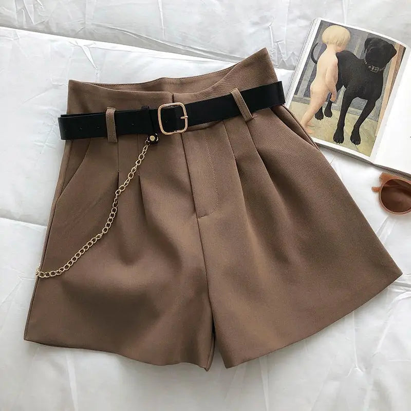 Brown shorts with a black belt and chain on a light gray surface.