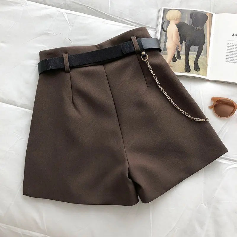 Brown shorts with a chain belt on a white surface, with a magazine featuring dog illustrations in the background.
