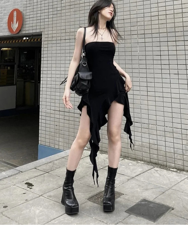 Woman in a black dress and boots standing against a tiled wall.