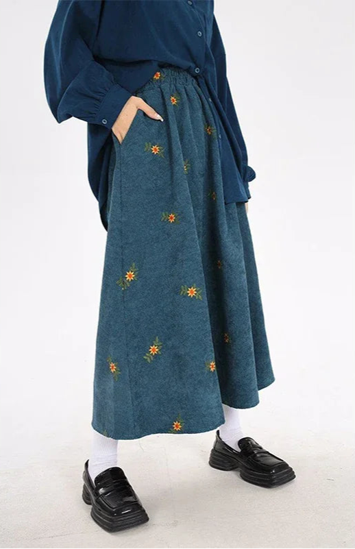 Person wearing a blue skirt with floral embroidery on a white background