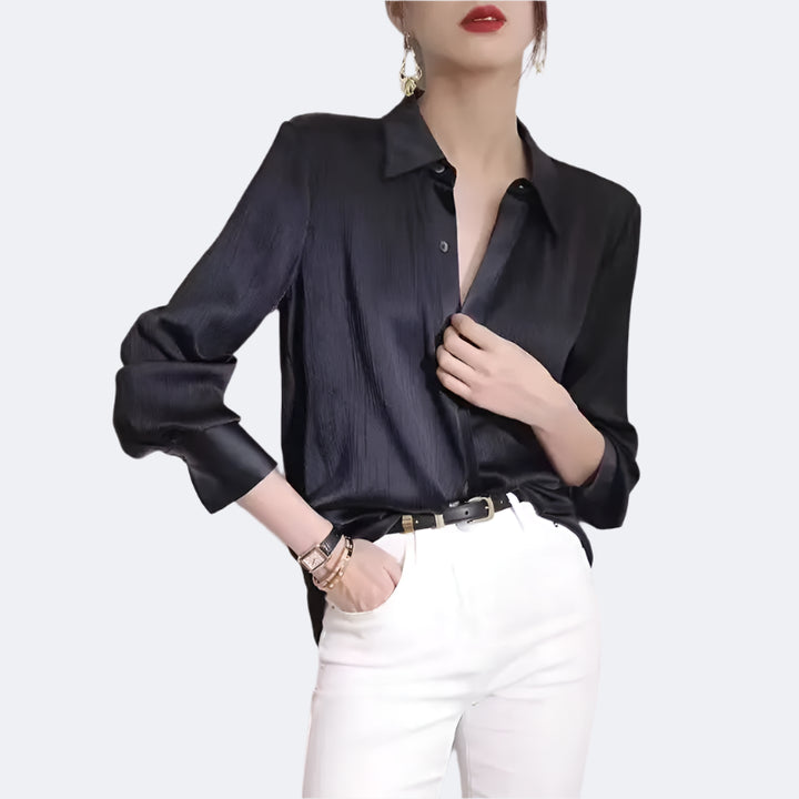 Person wearing a black satin shirt and white pants against a light background