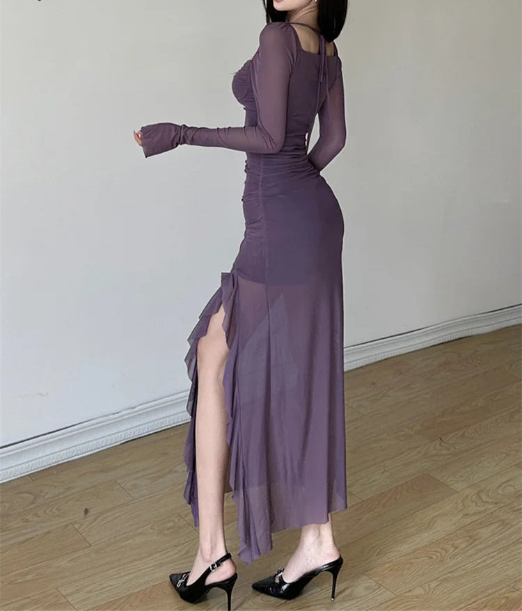 Woman wearing a long purple dress with a high slit, standing against a plain background.
