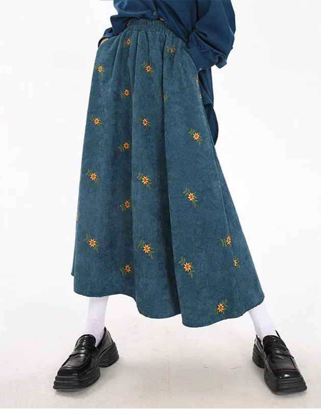 Person wearing a blue skirt with floral embroidery on a white background