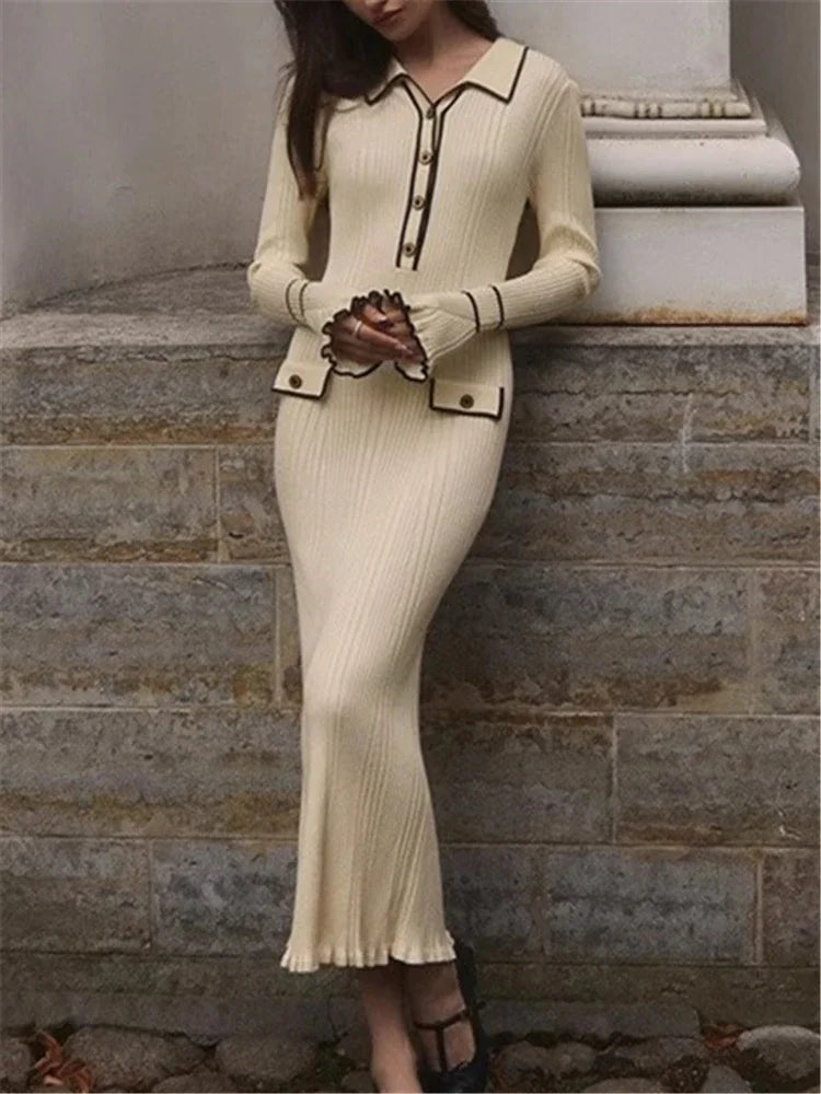 Woman wearing a beige ribbed dress with black trim against a stone wall.