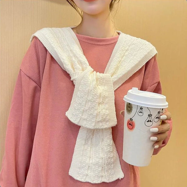 Person wearing a white knitted scarf holding a coffee cup against a beige background