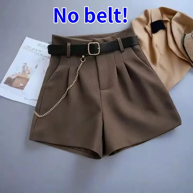Brown shorts with a black belt and gold chain on a gray surface.