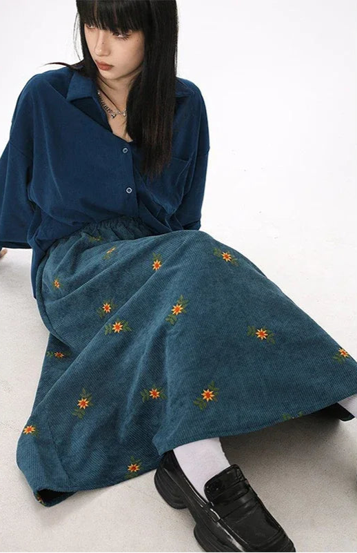 Woman wearing a blue dress with floral embroidery sitting on a white floor.