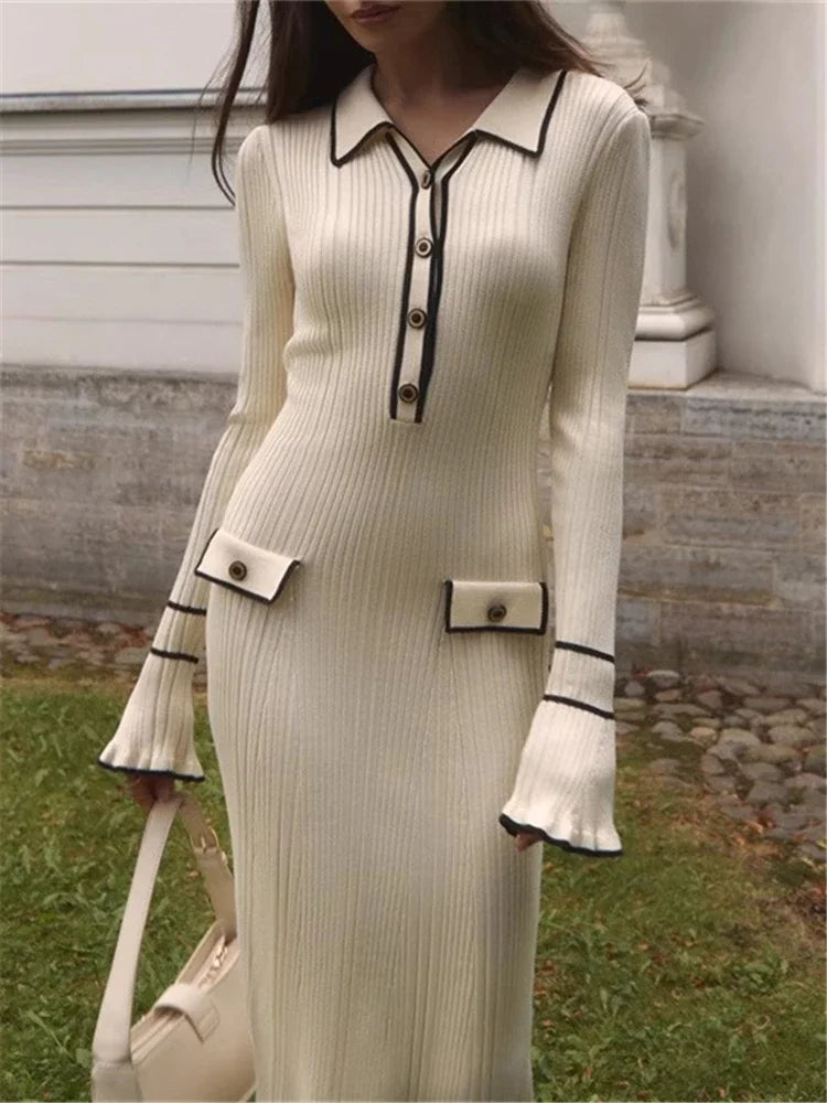 Woman wearing a long, cream-colored dress with black trim in an outdoor setting.