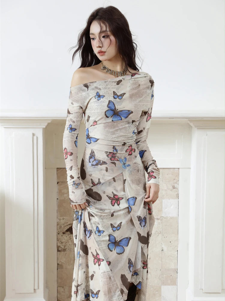 Woman wearing a long dress with butterfly pattern against a white wall.