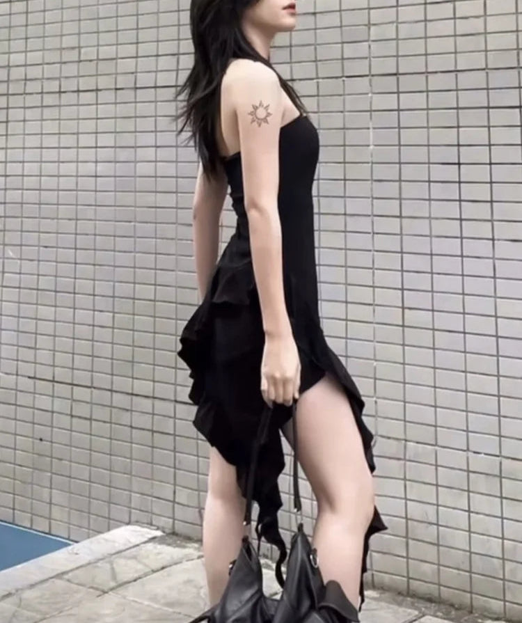 Woman wearing a black dress with ruffled details against a tiled wall.