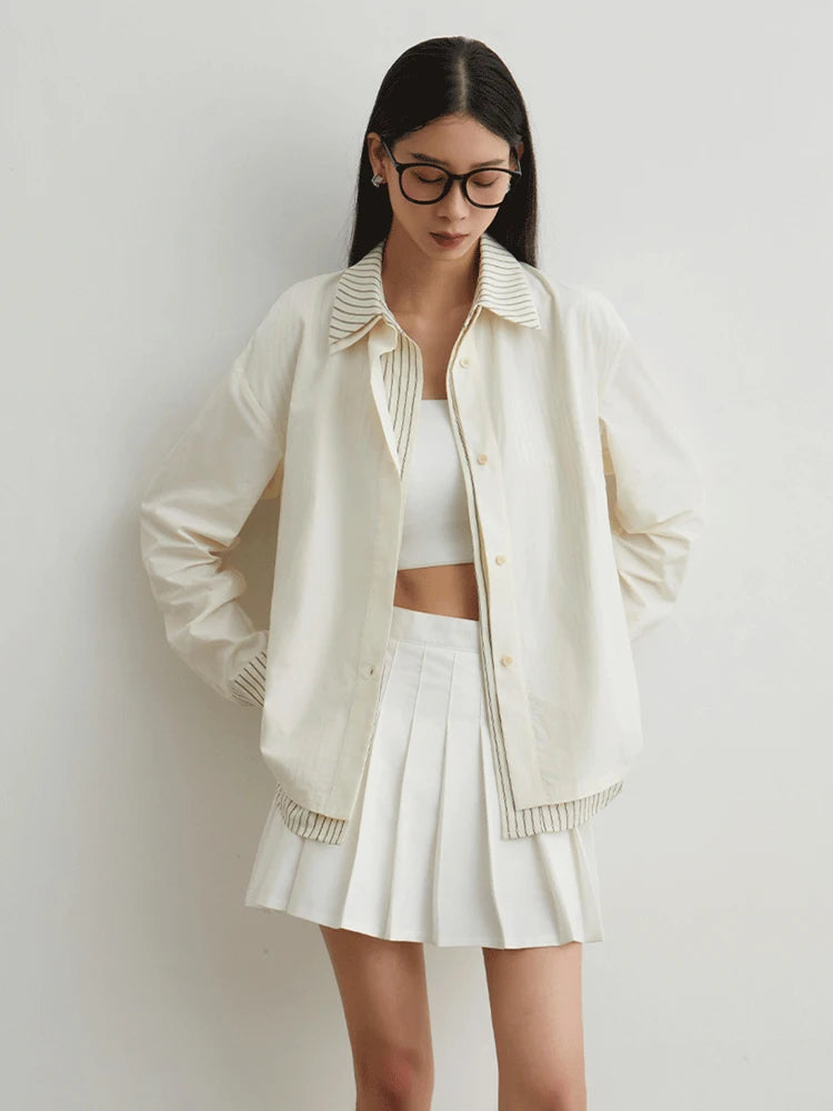 Woman wearing a cream-colored cardigan over a white top and skirt on a plain background