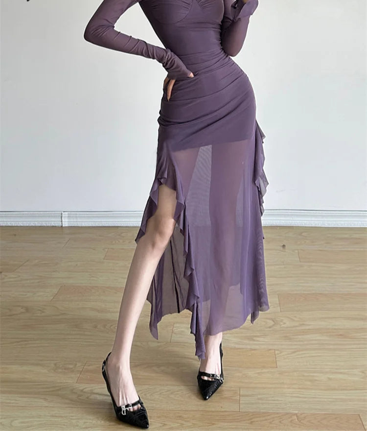 Woman wearing a long-sleeve purple dress with a slit on a wooden floor.