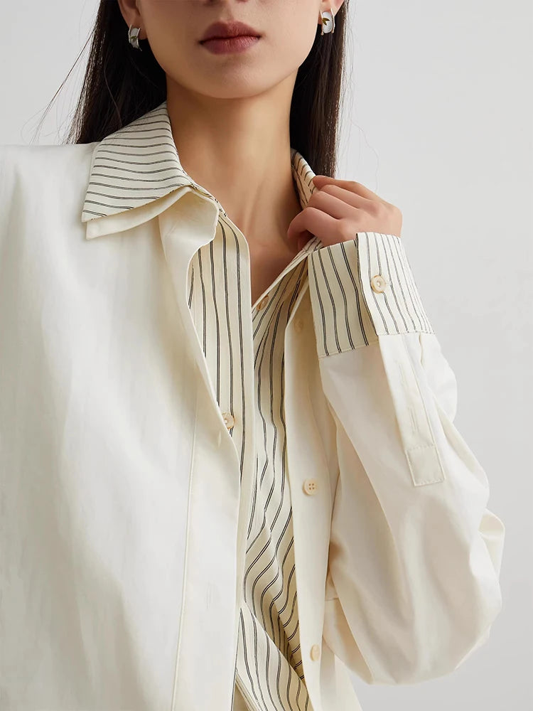 Close-up of a person wearing a white shirt with black striped details on a plain background